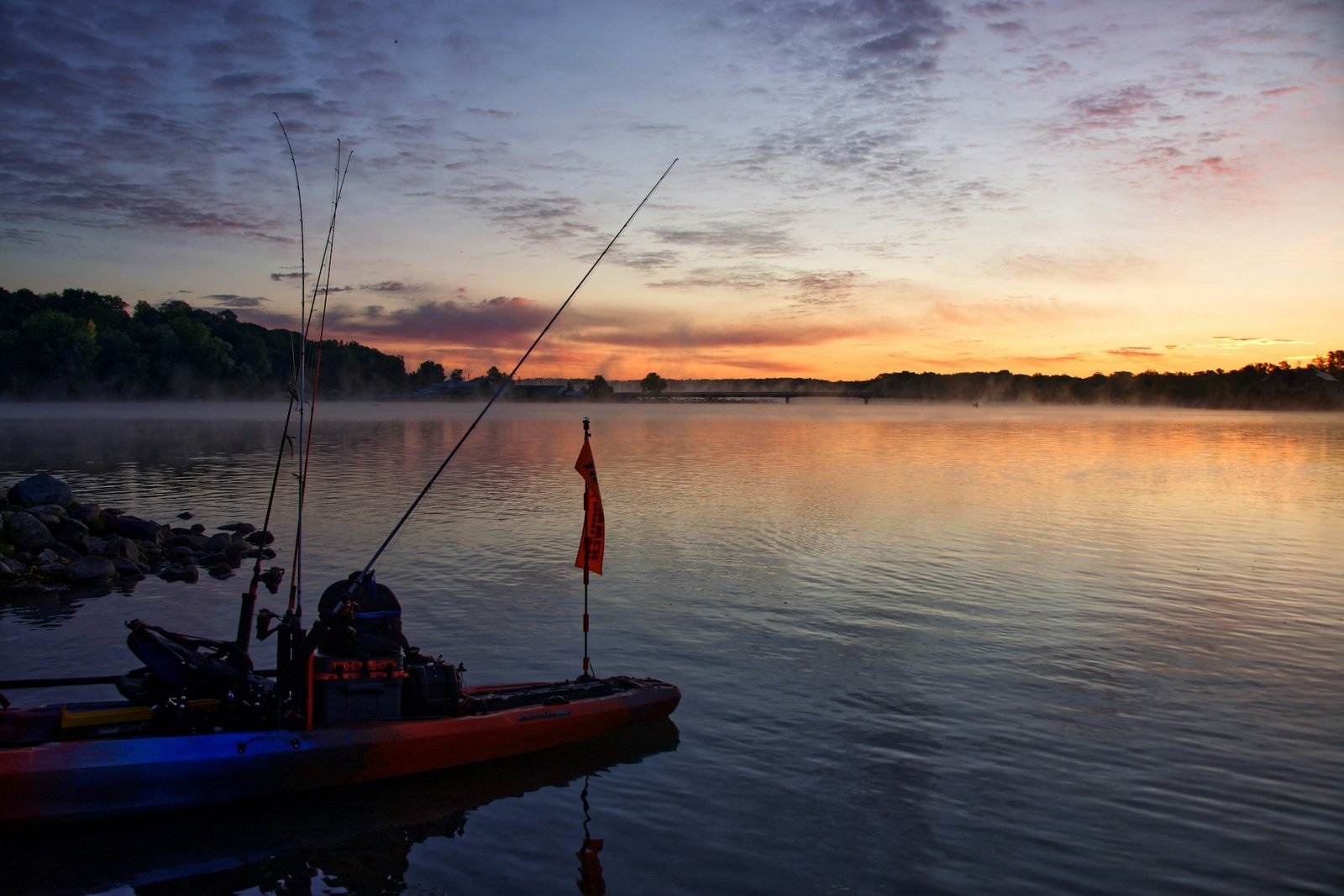 A serene morning on the river with a fishing rod resting against a boat, mist rising from the water.